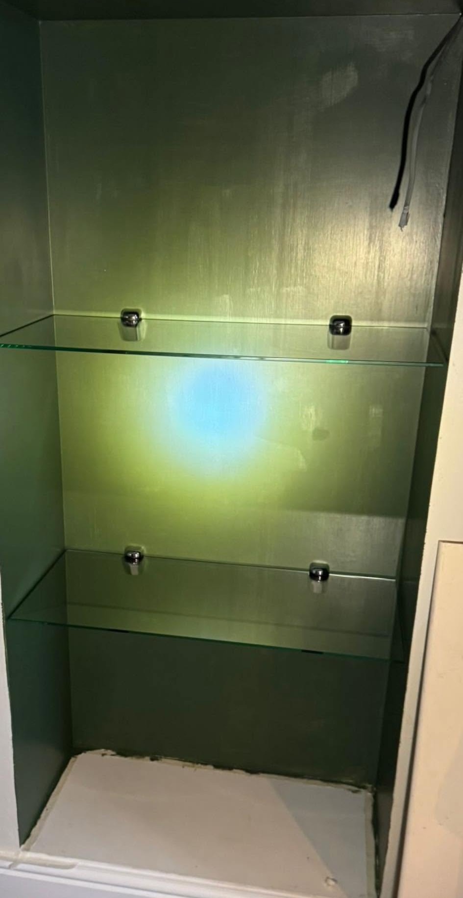 Glass shelves fitted inside a lit green display cabinet