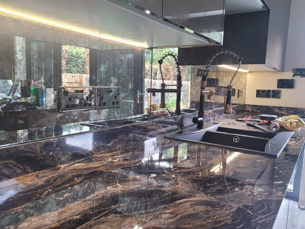 Mirrored glass splashback fitted behind a kitchen sink, reflecting the garden